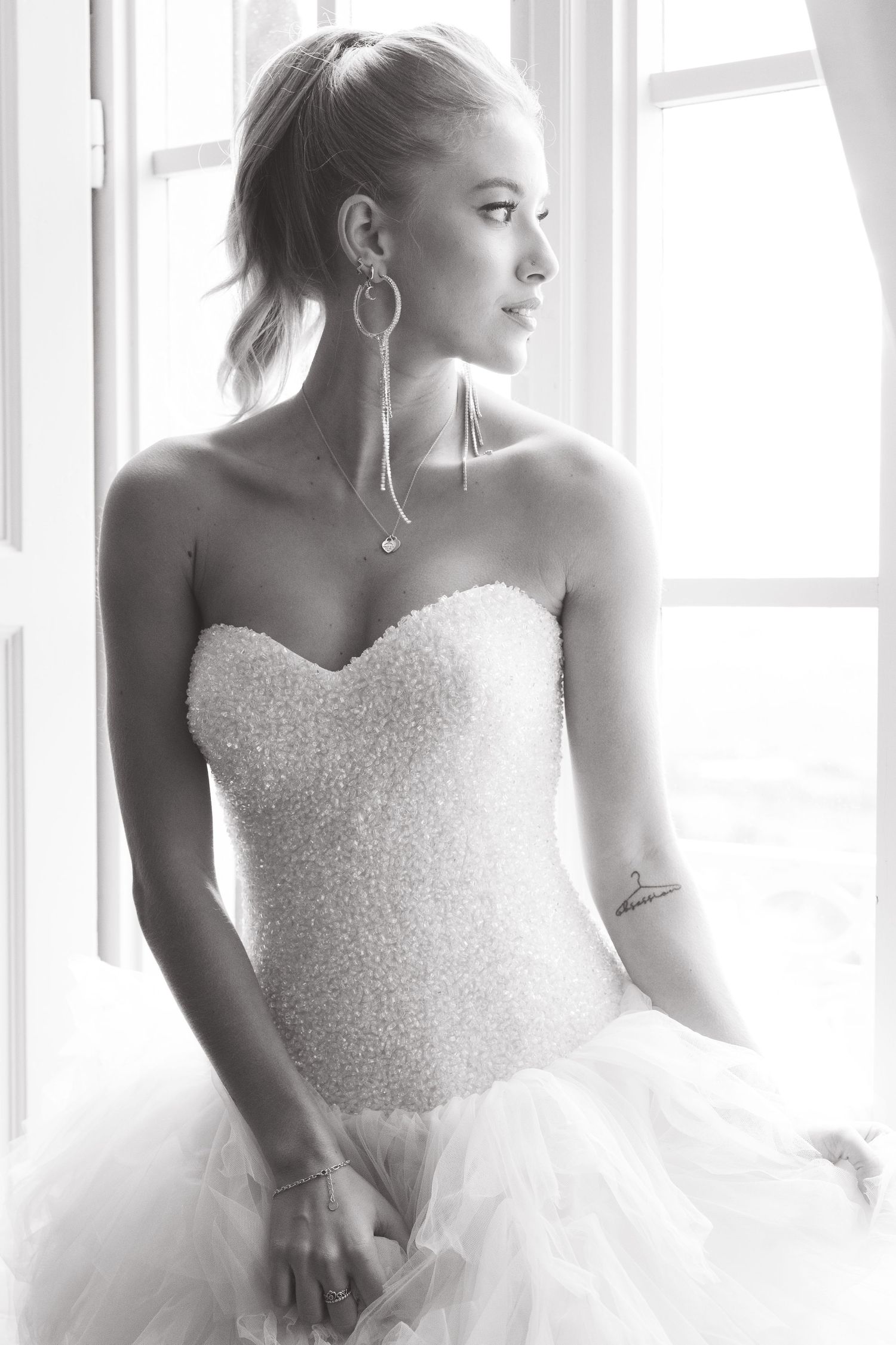 Black and white portrait of a bride in a strapless beaded wedding gown gazing out a window.