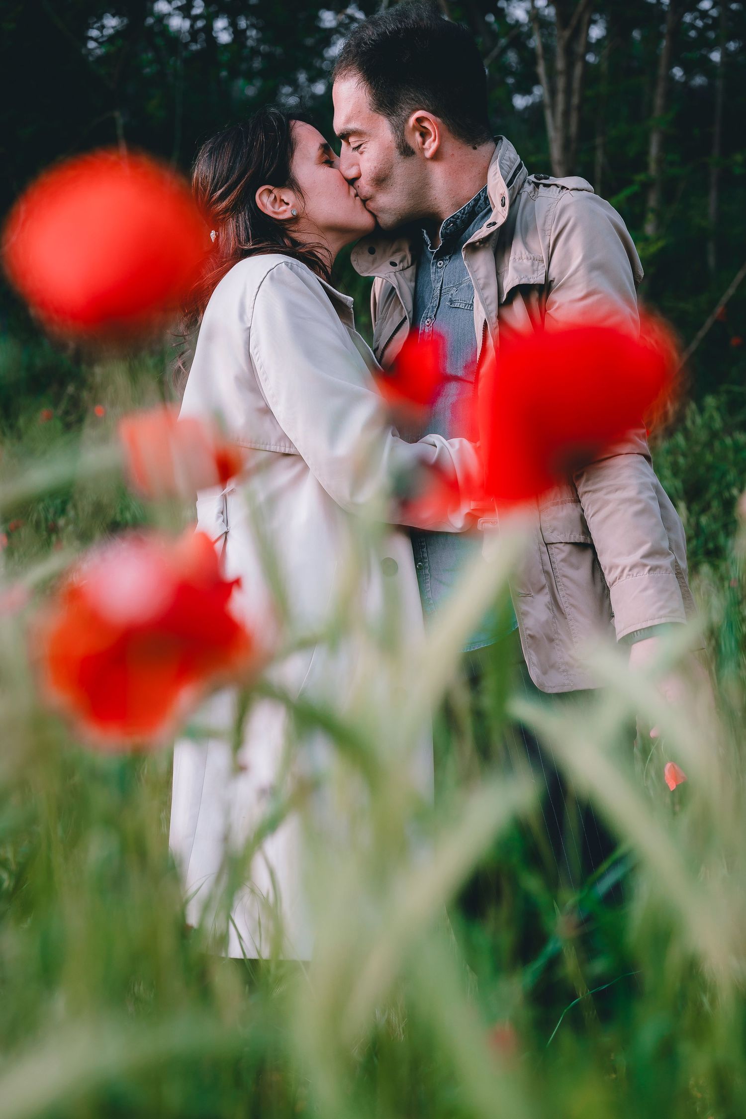 A romantic couple shares a tender kiss among vibrant red poppies in a dreamy outdoor setting.