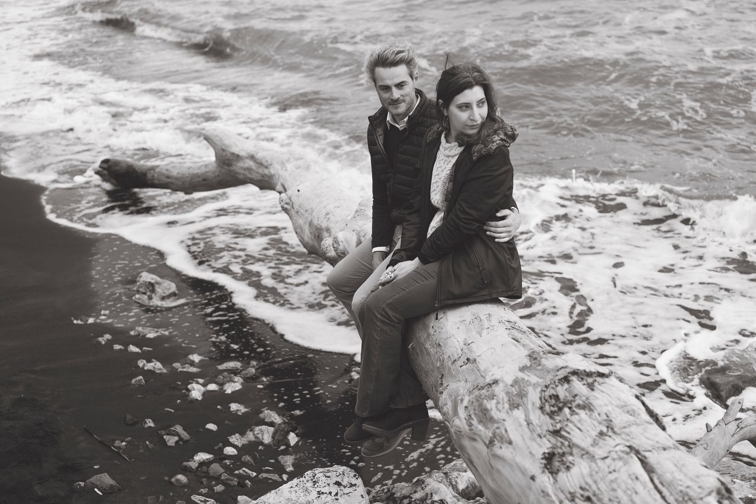 Vintage black and white photo of couple sitting on rocky coastline with crashing waves.