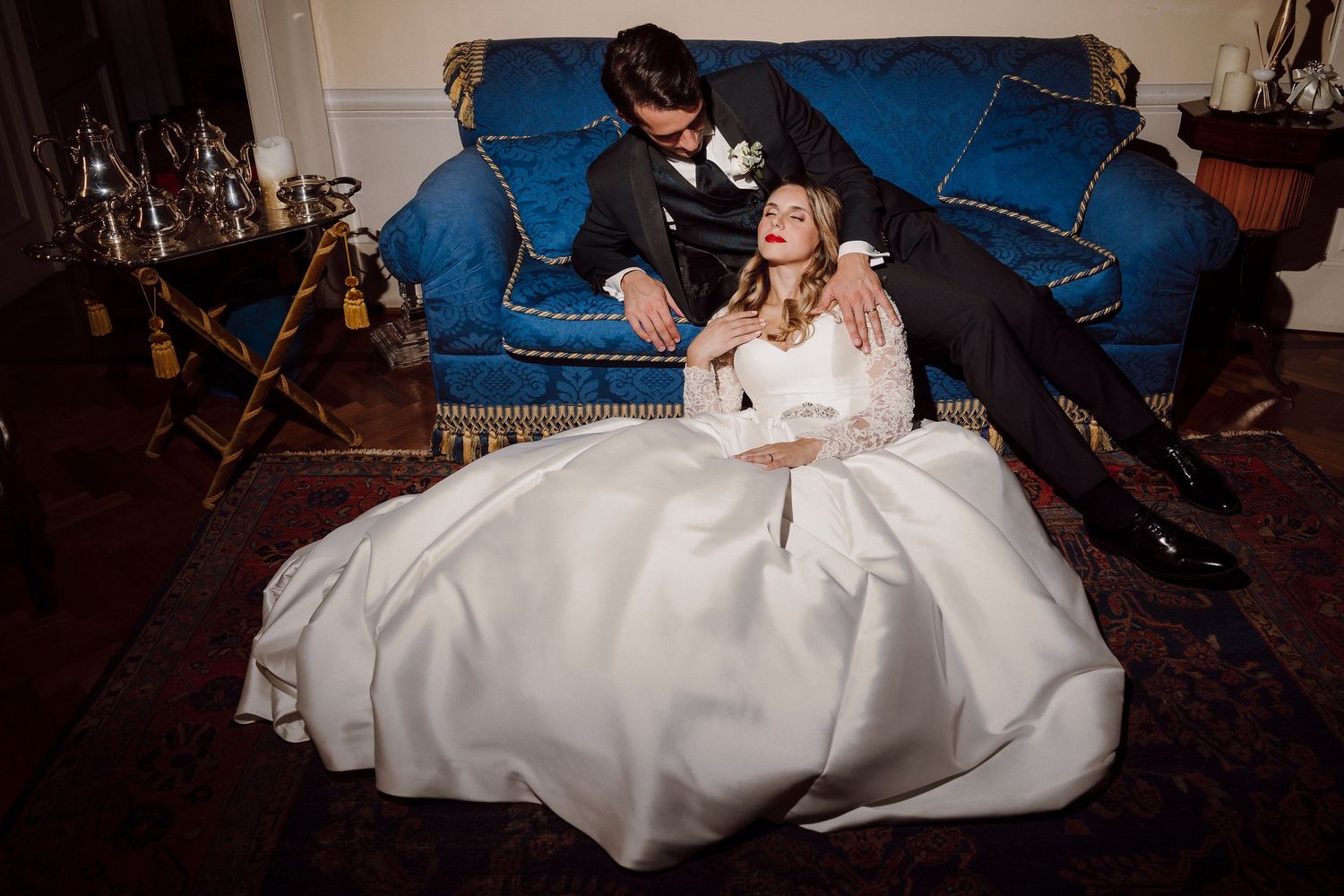 Intimate wedding moment captured on a blue velvet sofa in warm lighting.