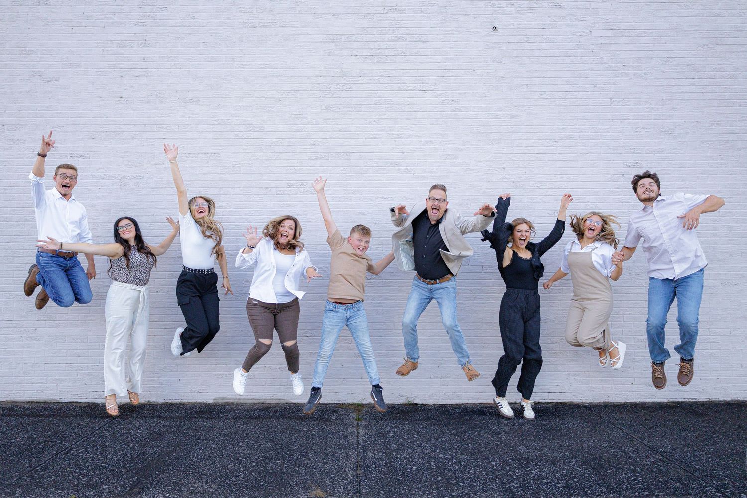 A group of people jumping together for a joyful photo against a light gray wall.
