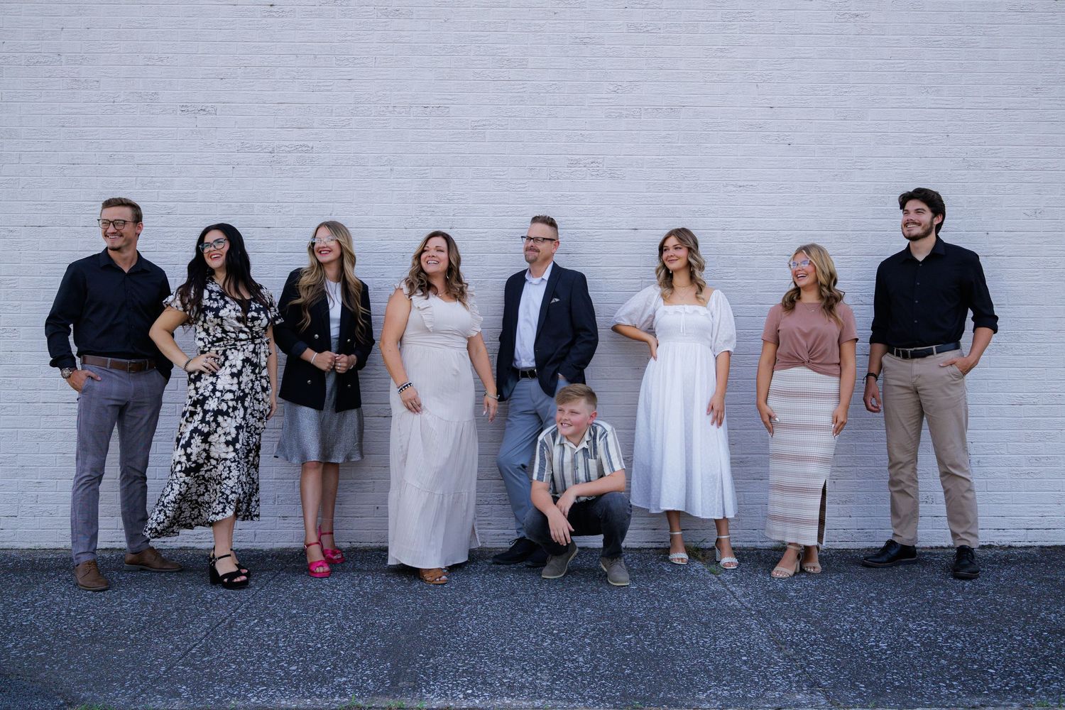 A group of people dressed in formal attire pose together against a white wall outdoors.