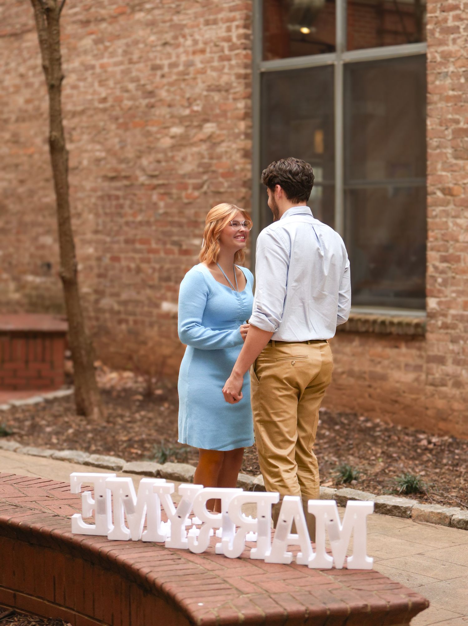 Couple stands by decorative lettering during outdoor engagement moment.