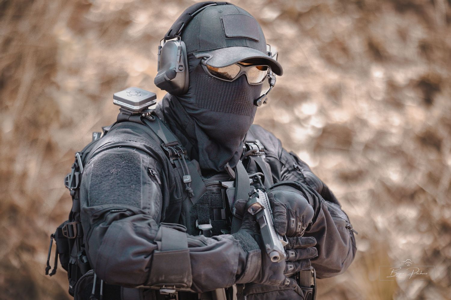 Tactical operator in full black gear with protective mask and hearing protection.