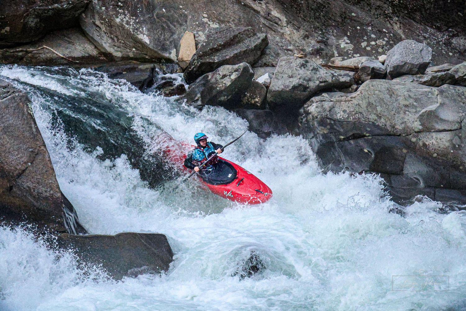 Kayaker navigating through white water rapids between rocky cliffs.