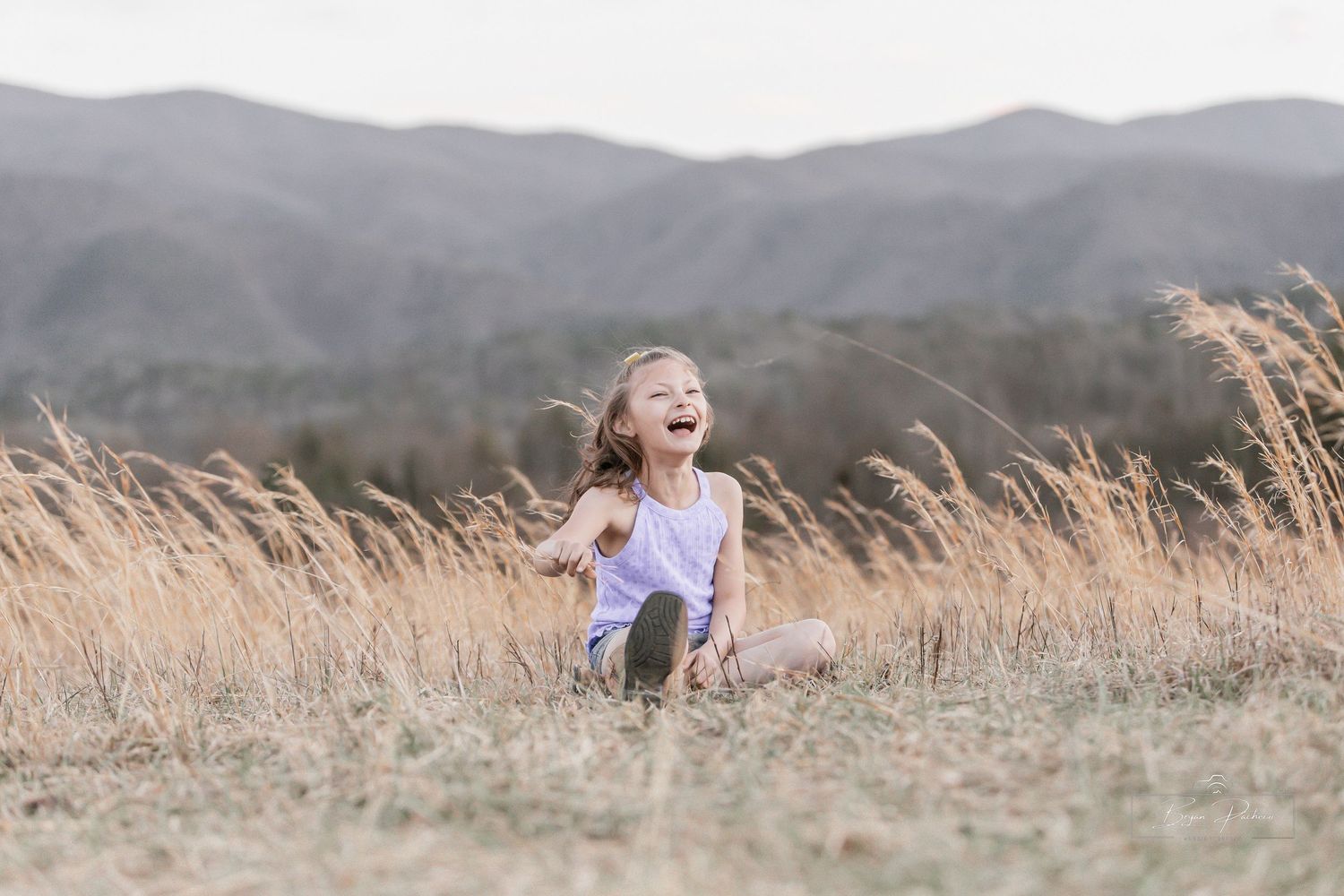 Child playing in golden field with mountains visible in background.