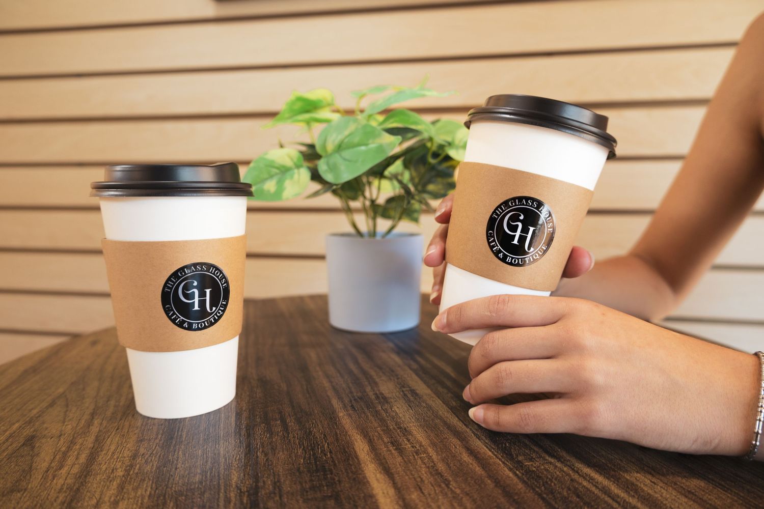 Two disposable coffee cups with black Cafe 41 logo branding on wooden table with small green plant in background.