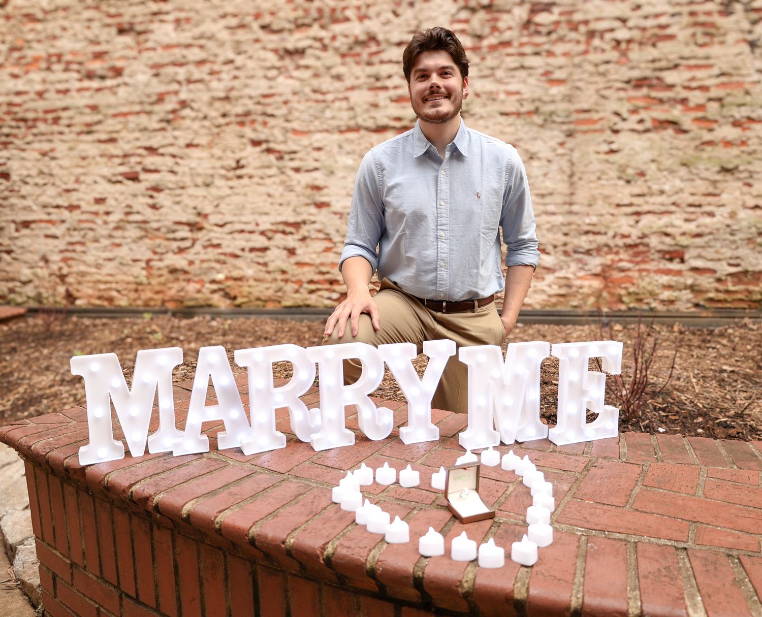 Creative marriage proposal setup with white letters spelling 'Marry Me' on brick wall.