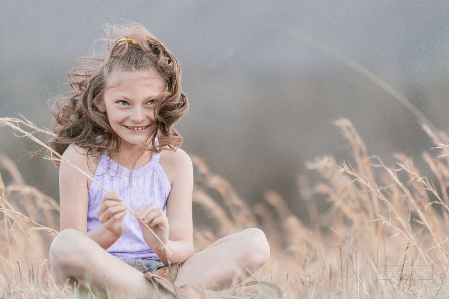 Child sitting cross-legged in field with mountains in distance.