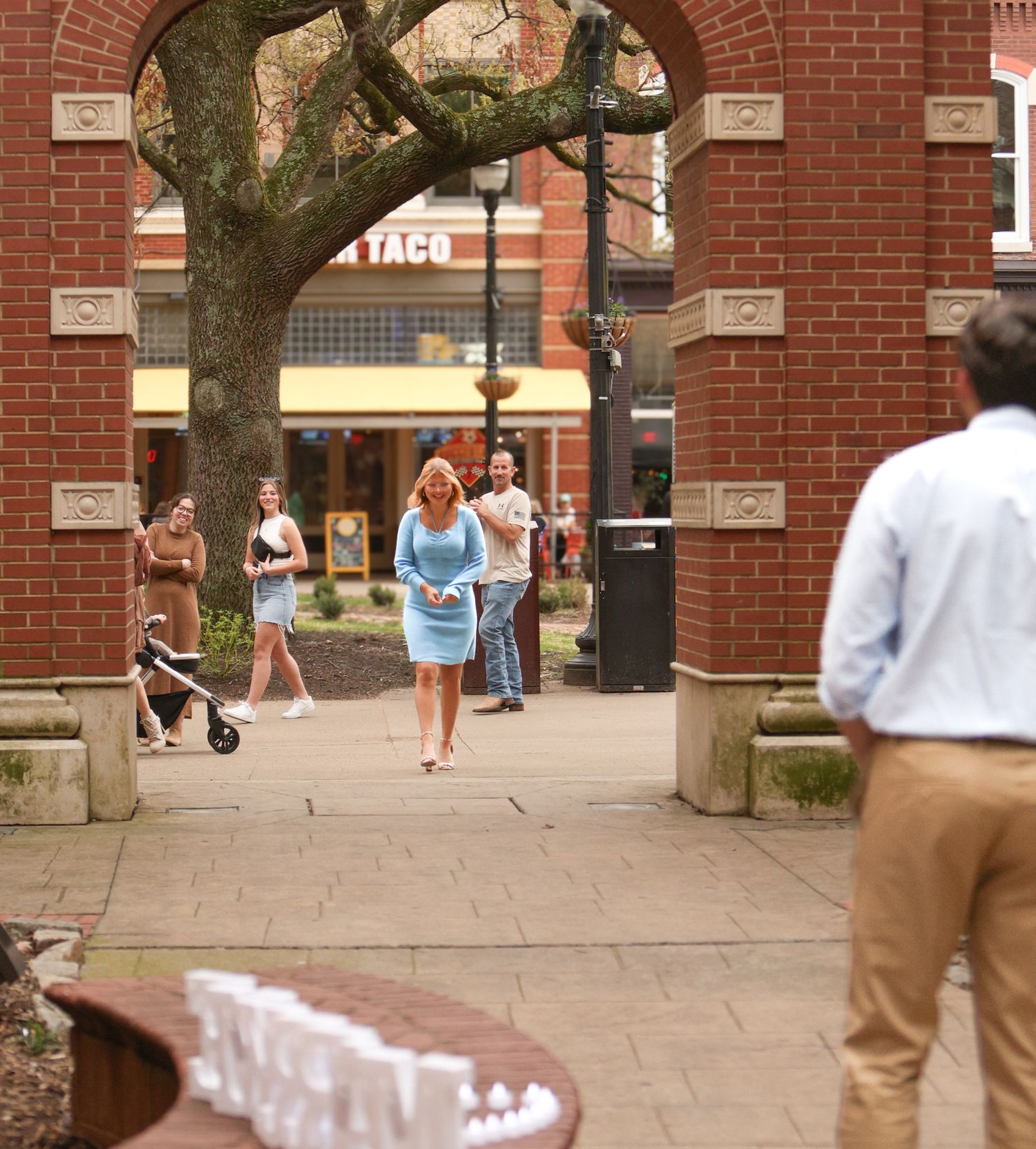 Woman walks through brick archway during surprise proposal setup.