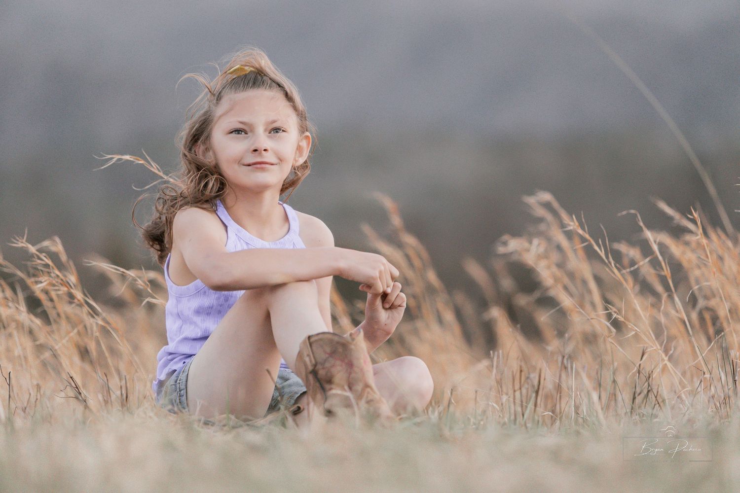 A child sits with a stuffed animal in golden grass at sunset.