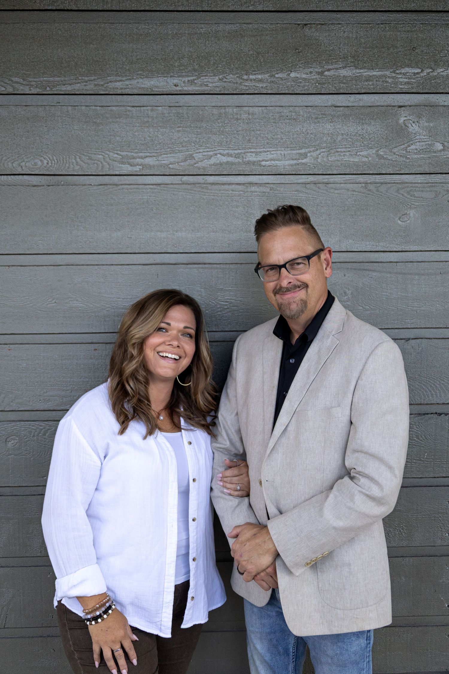 A couple in white and gray sharing playful candid moments against a rustic wooden wall.
