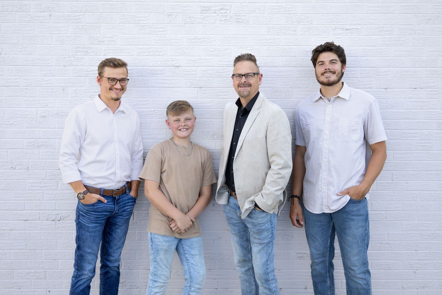 Four people in casual clothing standing together against a white wall.
