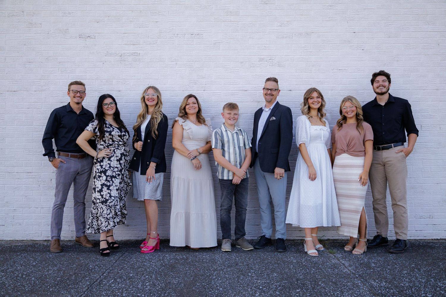 A group of people in coordinating light colored outfits posed casually against a white wall.