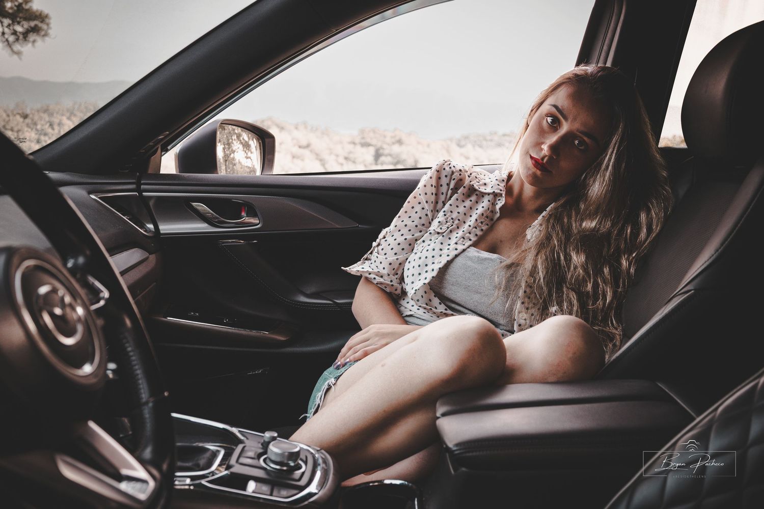 Person sleeping in reclined car seat while wearing wireless earbuds and sunglasses during daytime.