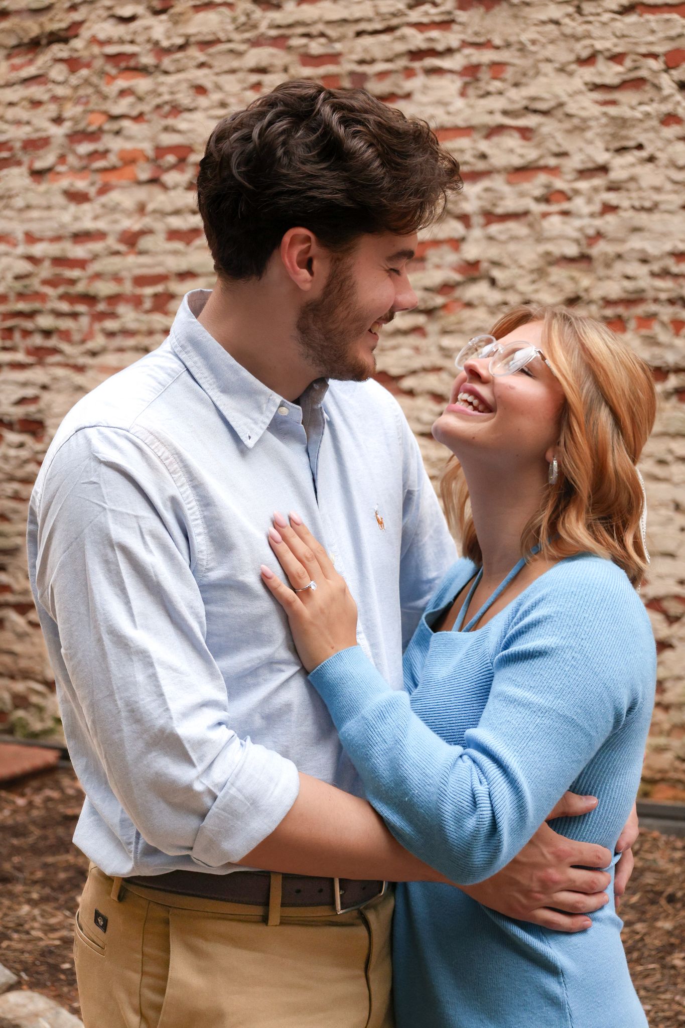 Couple shares loving moment against rustic brick wall backdrop during photo session.