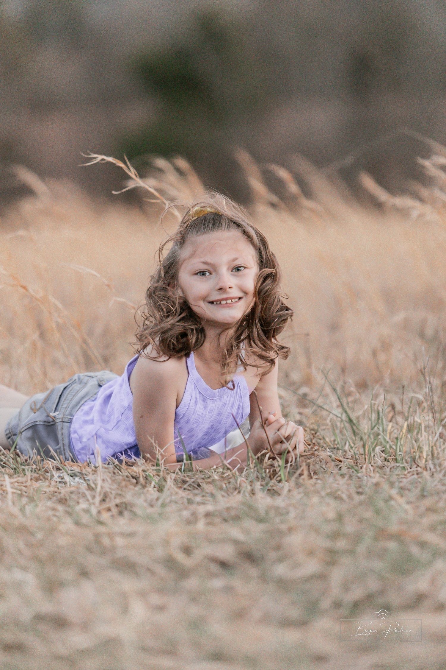 A child in a purple dress lies in tall grass on a sunny day.
