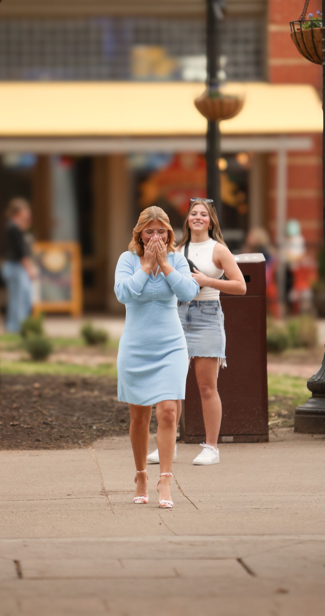 Woman in light blue dress reacts with surprise during outdoor proposal moment.