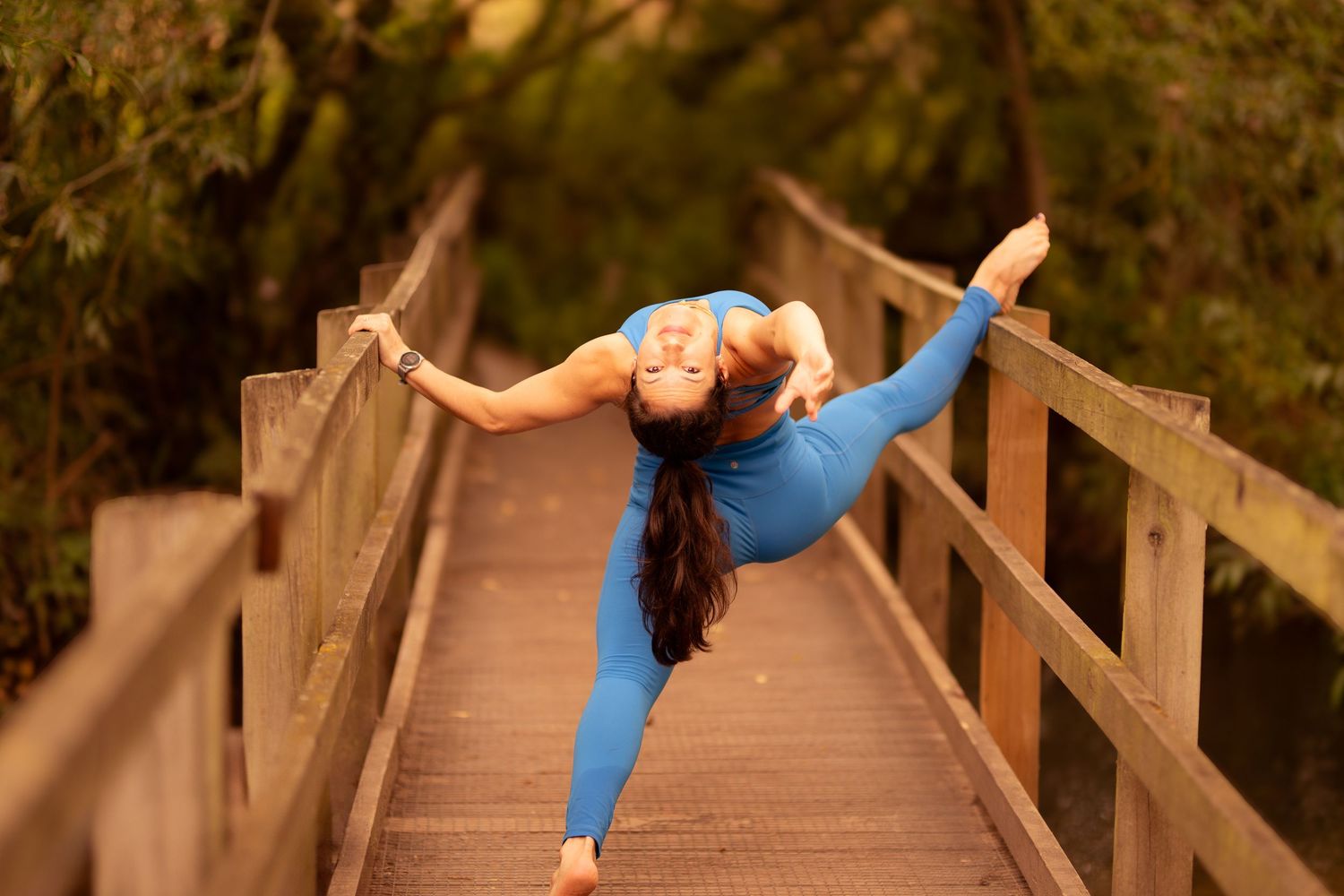 Person in blue top performs precise dance movements on wooden boardwalk in nature setting.