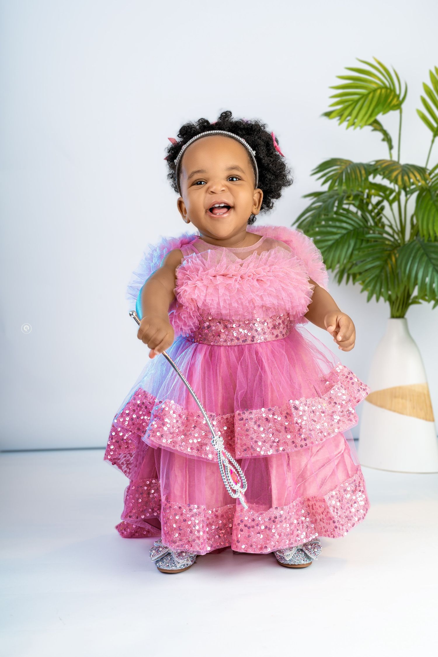 Baby in a sparkly pink tulle dress sitting against a white background with tropical plants.