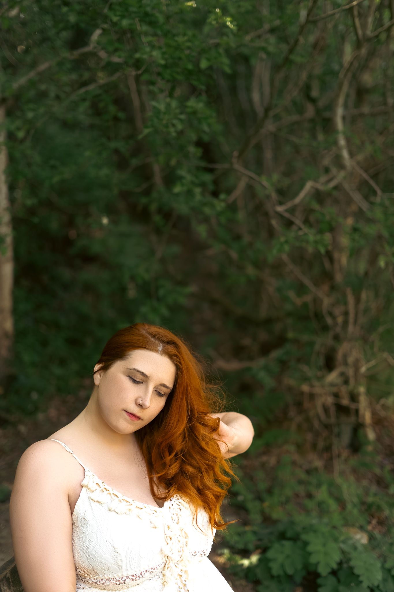 A dreamy portrait in a white lace dress against a lush green forest background.