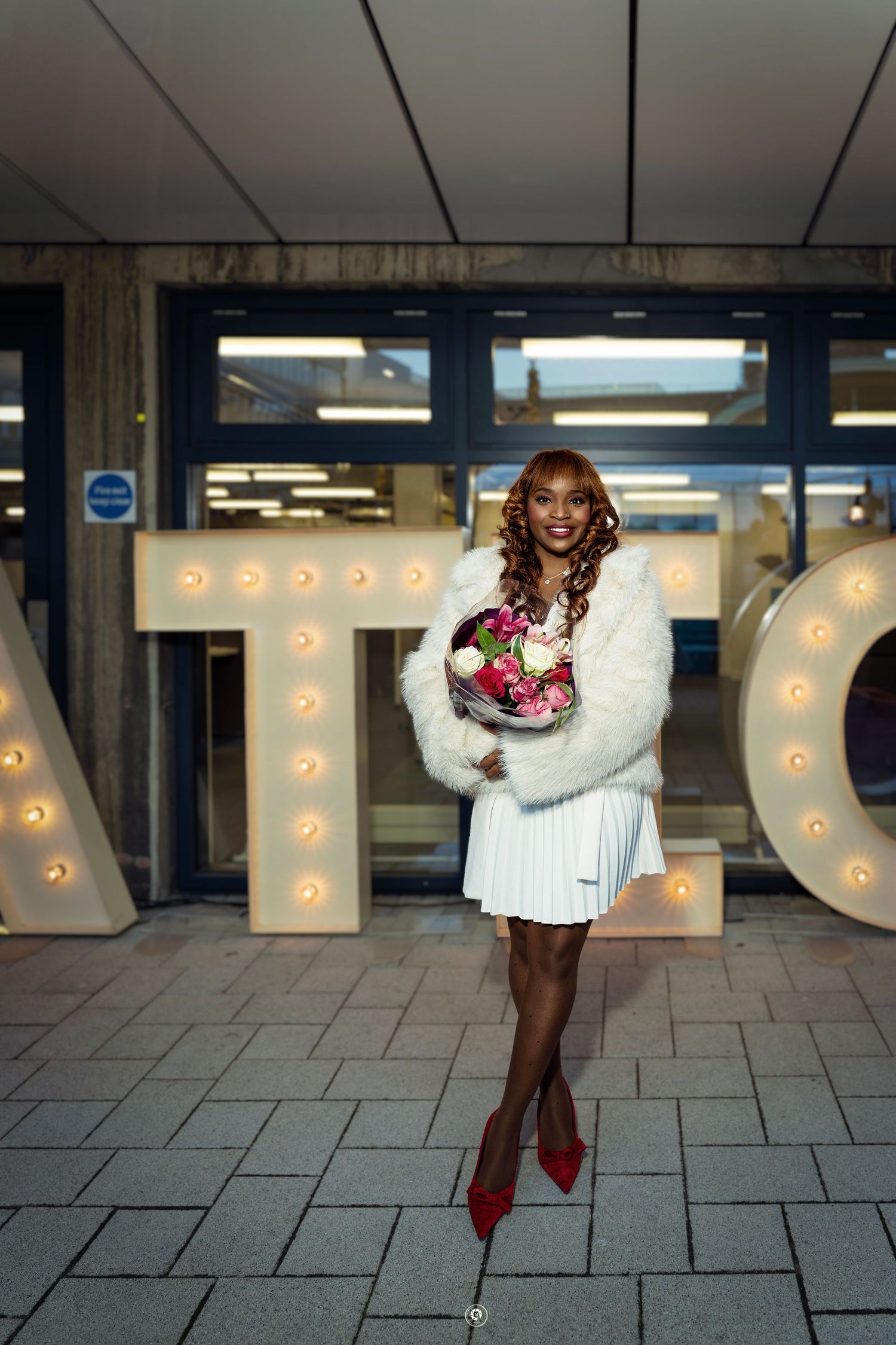A stylish winter look featuring a white sweater dress, red heels and decorative light-up letters in the background.