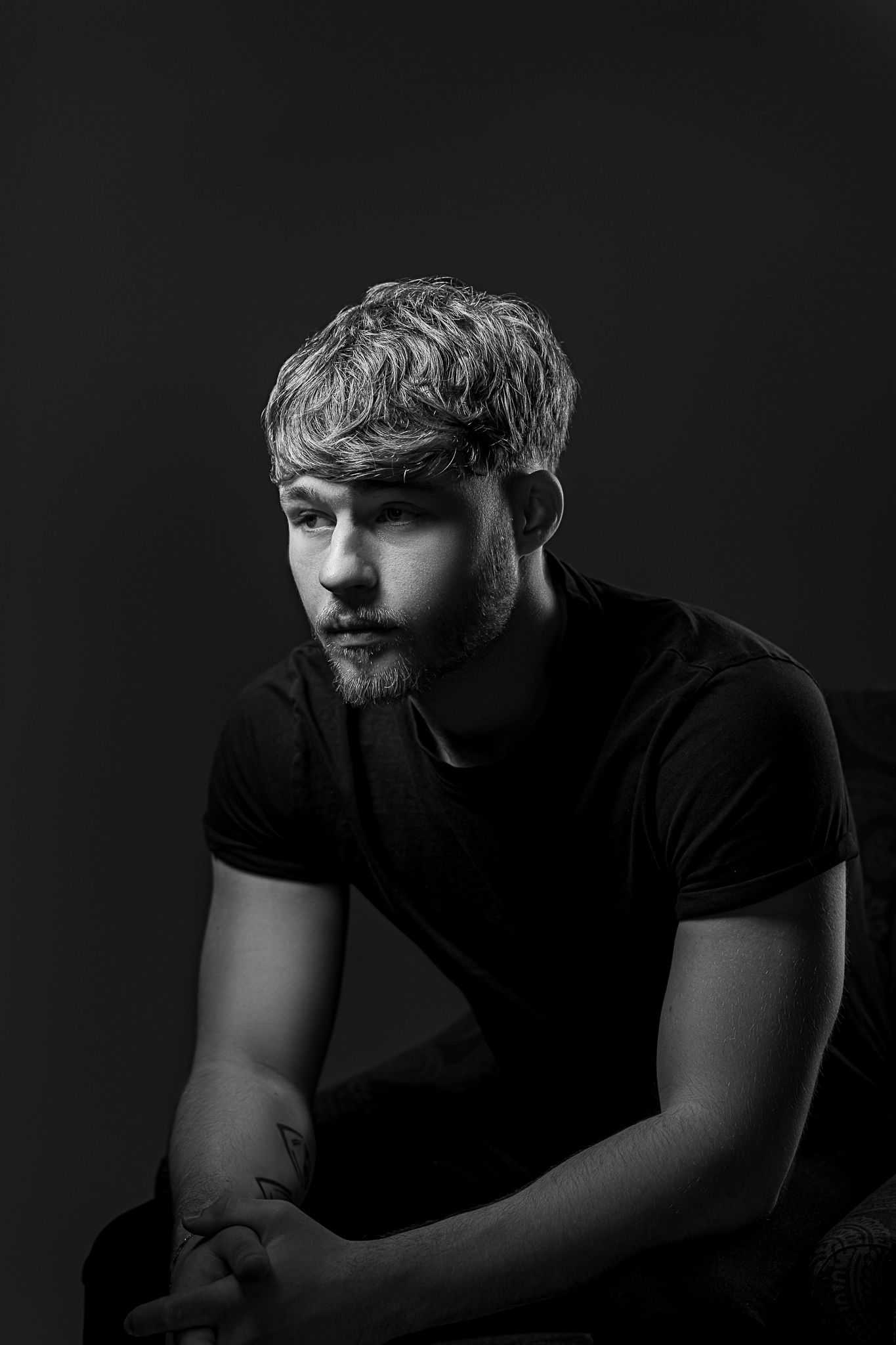 Dramatic black and white portrait of someone in a dark t-shirt with dramatic side lighting against a dark background.