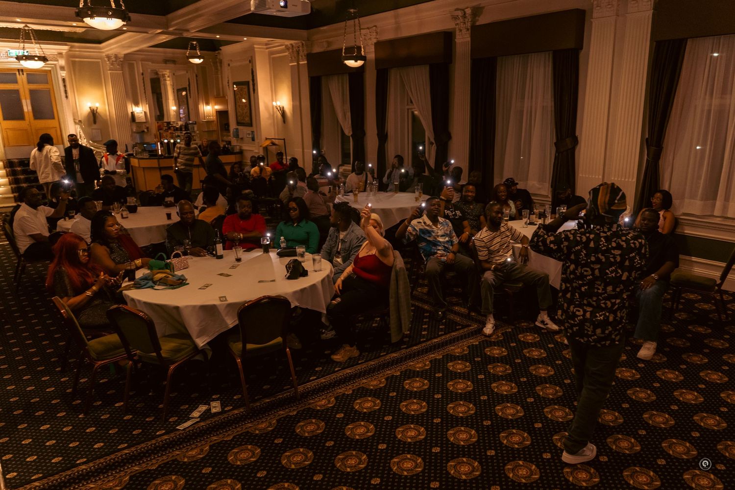 A dimly lit banquet hall with elegant chandeliers and round tables set up for a formal evening event.