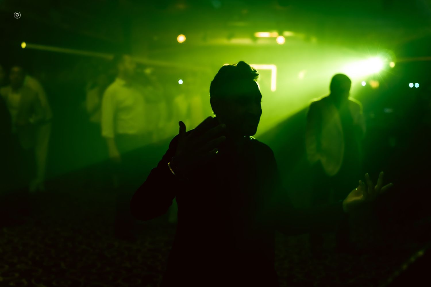 Green laser lights illuminate a dark nightclub dance floor with silhouetted figures dancing in the smoky atmosphere.