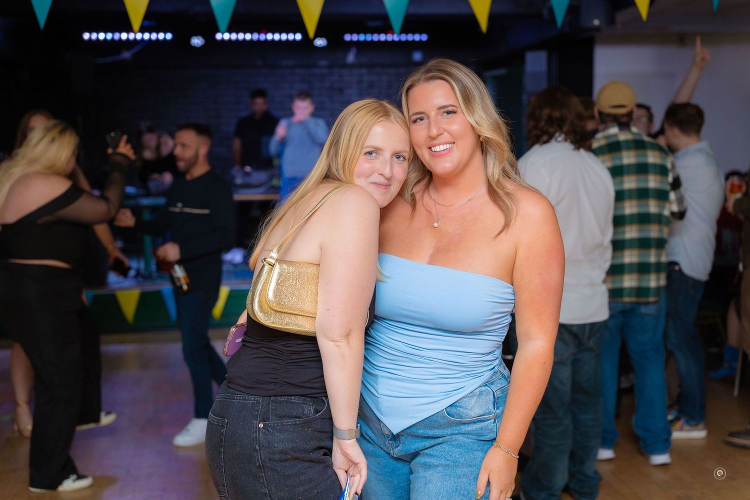 Partygoers dance and celebrate at a festive event with colorful bunting flags hanging overhead.