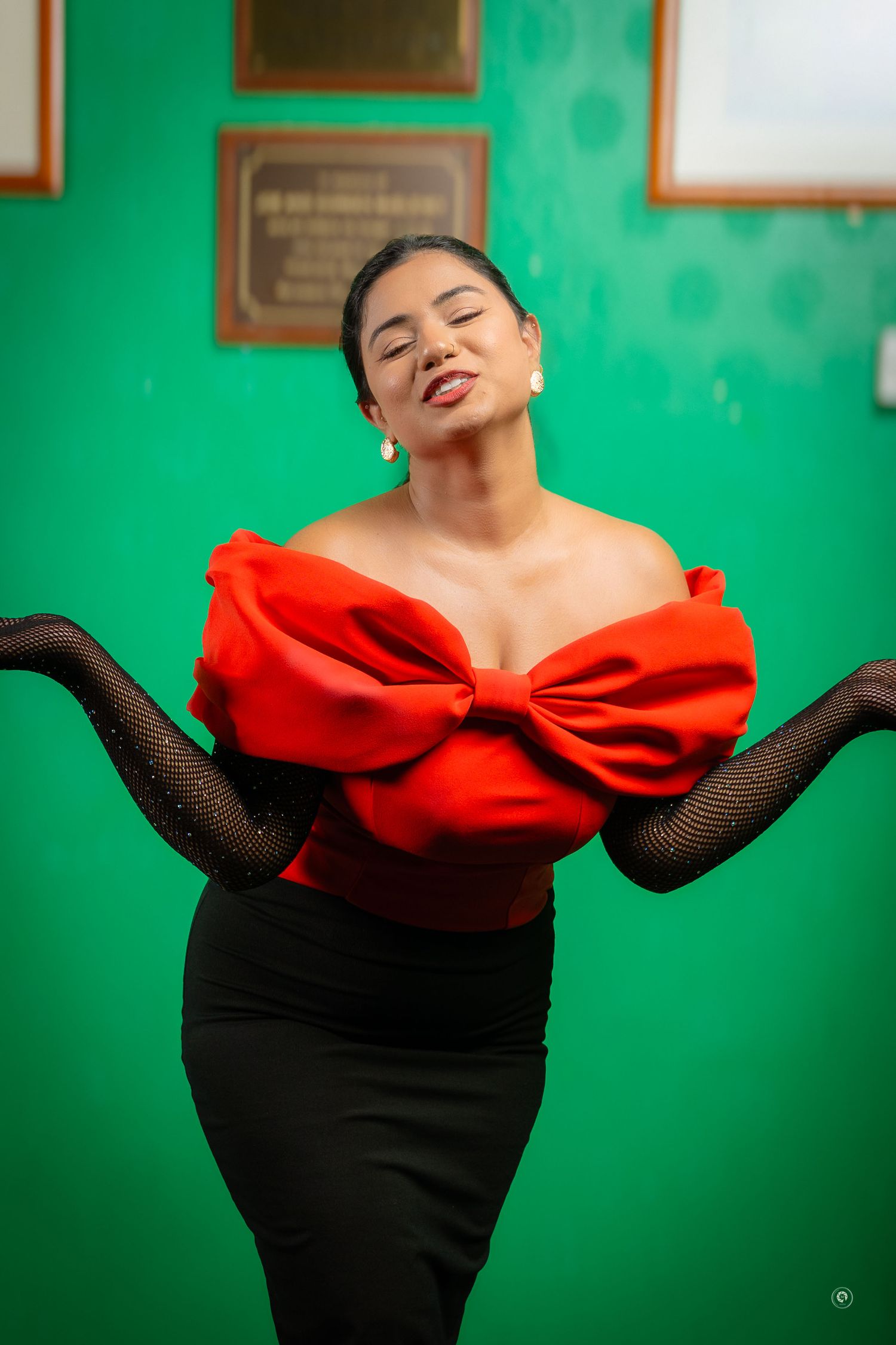 A series of fashion poses showing a dramatic black dress with a bold red bow against a vibrant green wall.