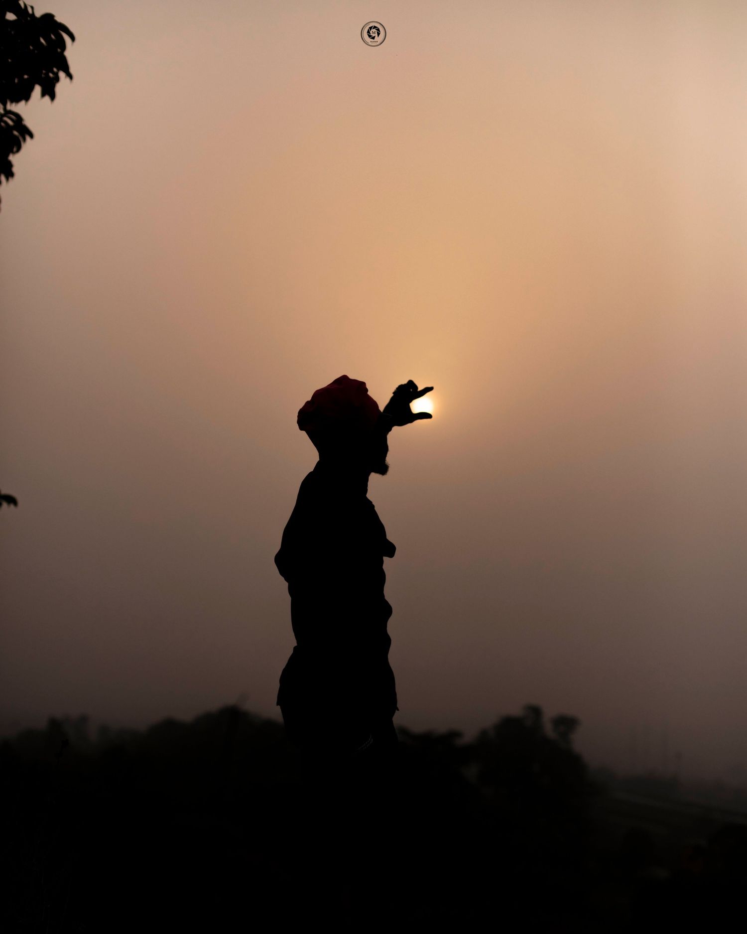 Silhouette of a person standing against sunset sky appearing to hold the sun between their fingers in creative perspective shot.