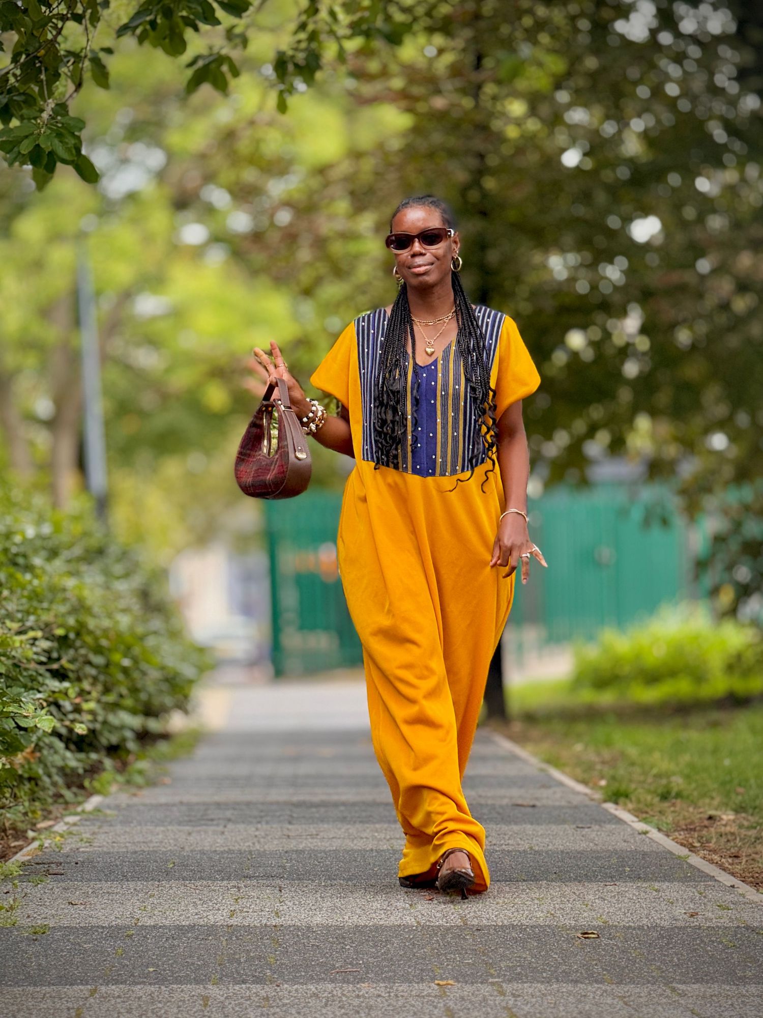 A person in a bright yellow outfit and striped vest walks down a tree-lined path while holding a football.
