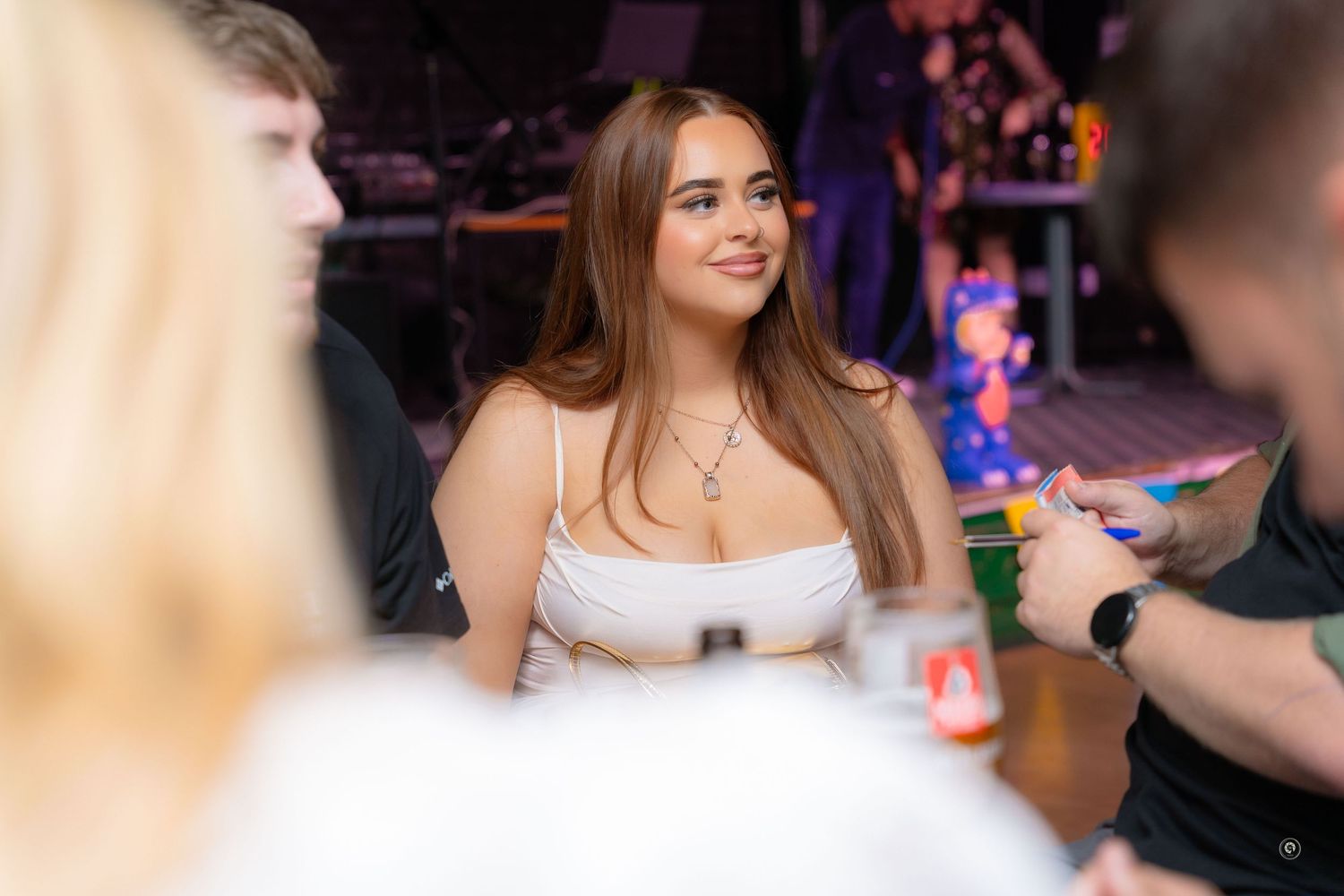 A group of friends enjoying drinks and conversation at a lively bar with colorful lighting in the background.