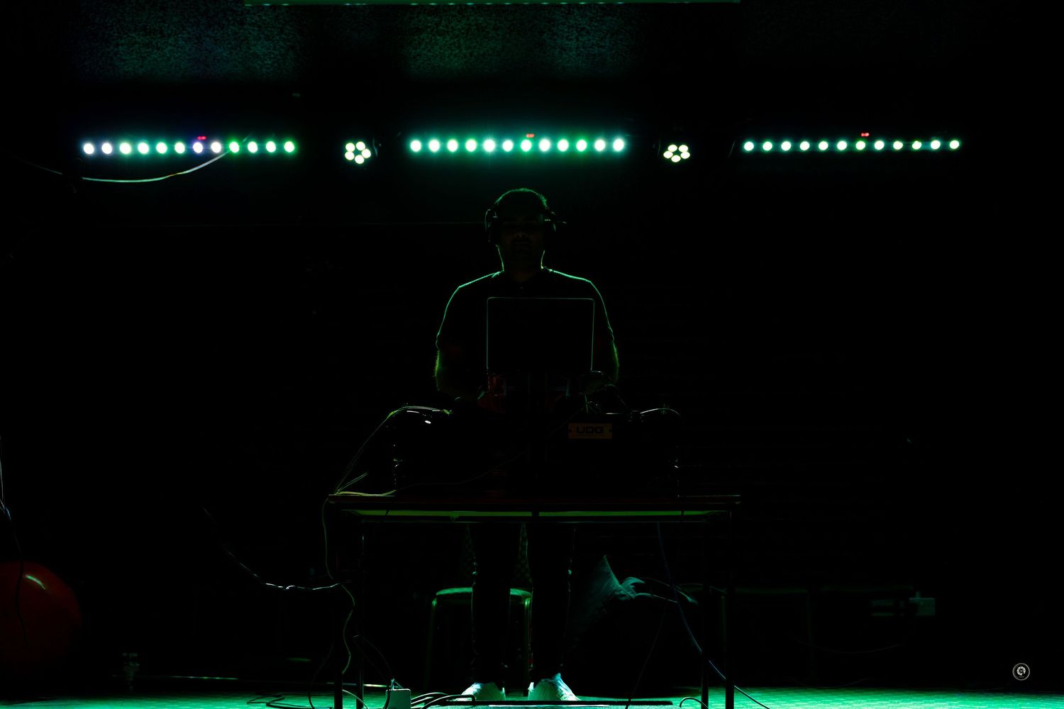 Green LED lights illuminate a dark performance stage with silhouetted figures and equipment visible.
