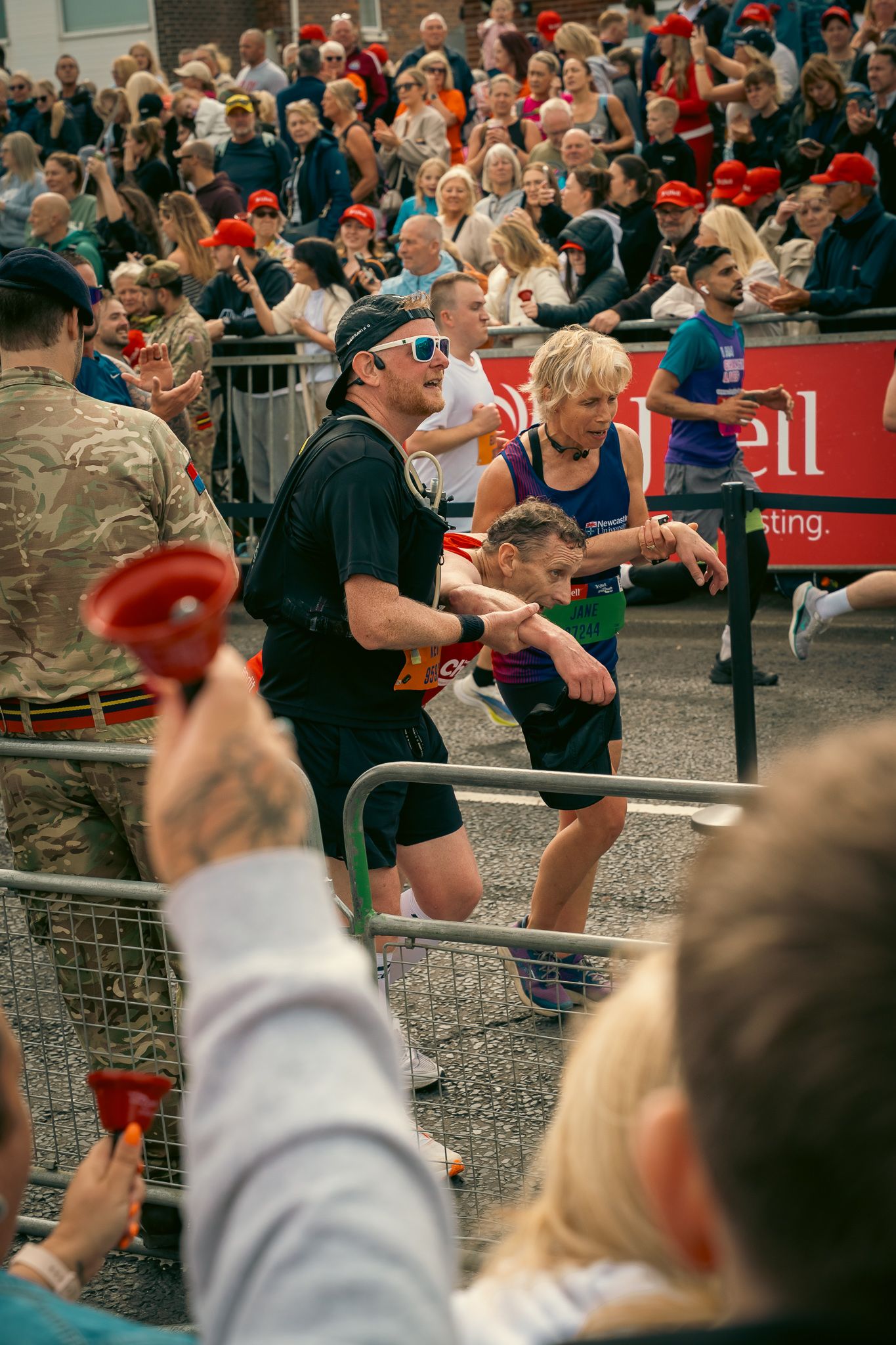 Crowd of spectators watching an outdoor sporting event through metal barriers at a public venue.