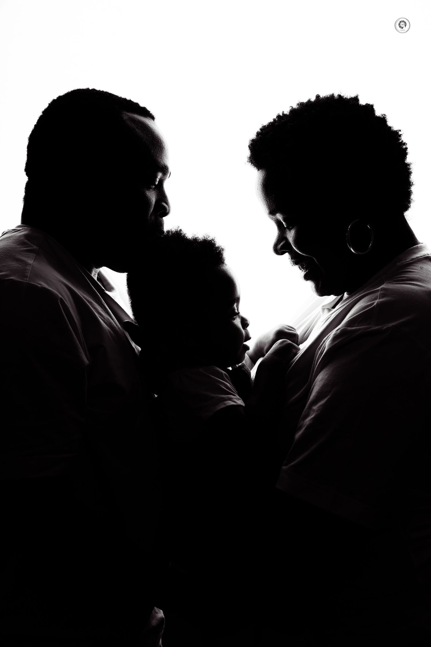 A dramatic black and white silhouette portrait of a family of three huddled close together in an intimate moment.