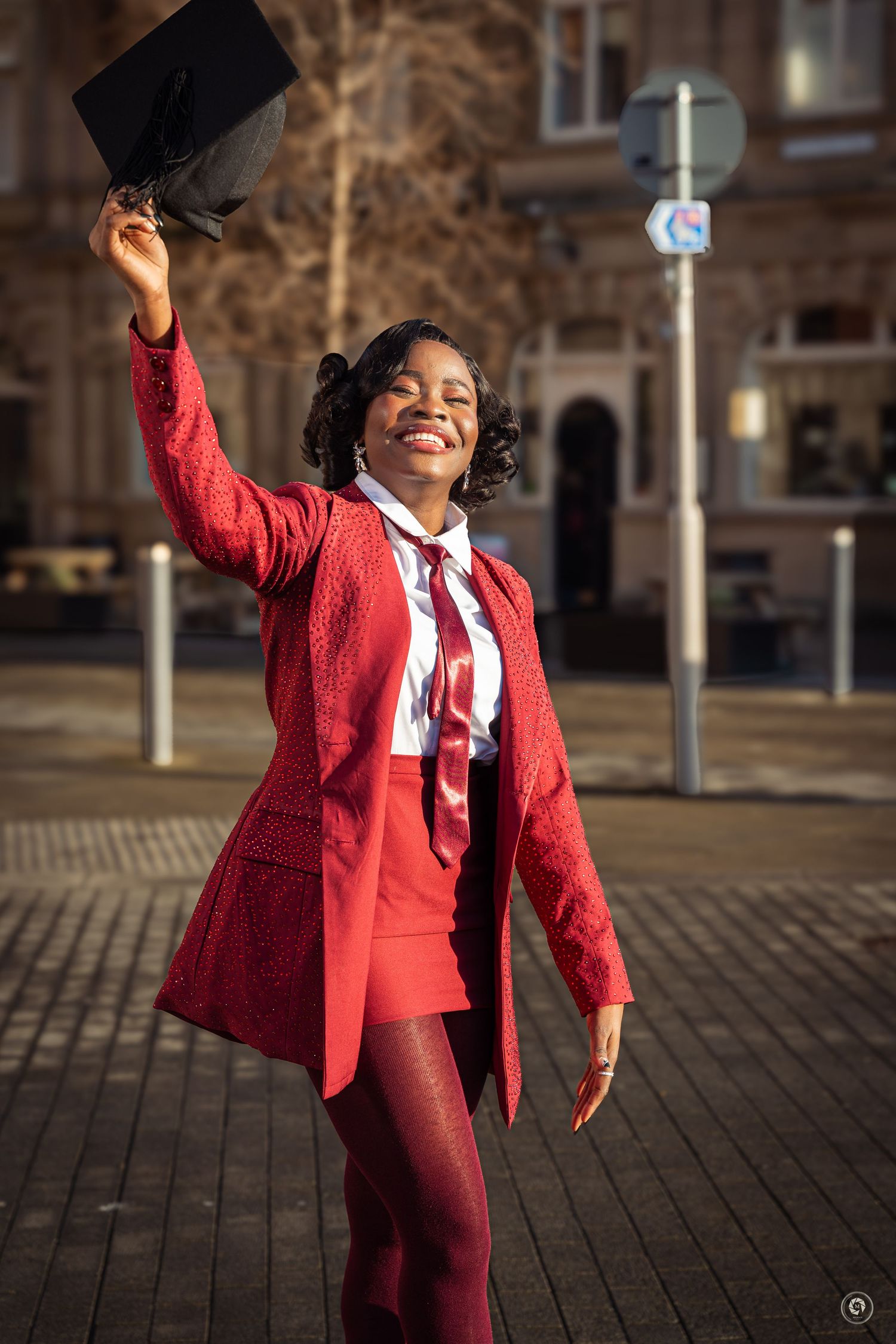 A person in a bright red suit and white shirt dances joyfully outdoors on a cobblestone street.
