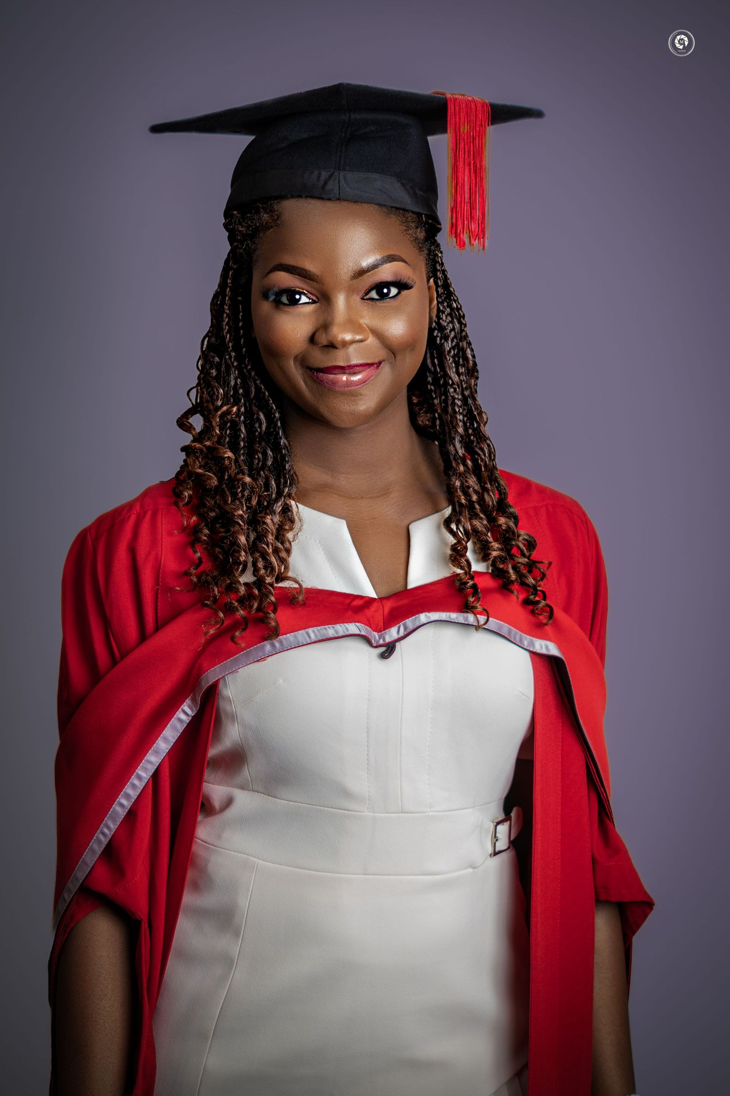 Graduate in red cap and gown with white collar smiles in professional portrait series against gray background.