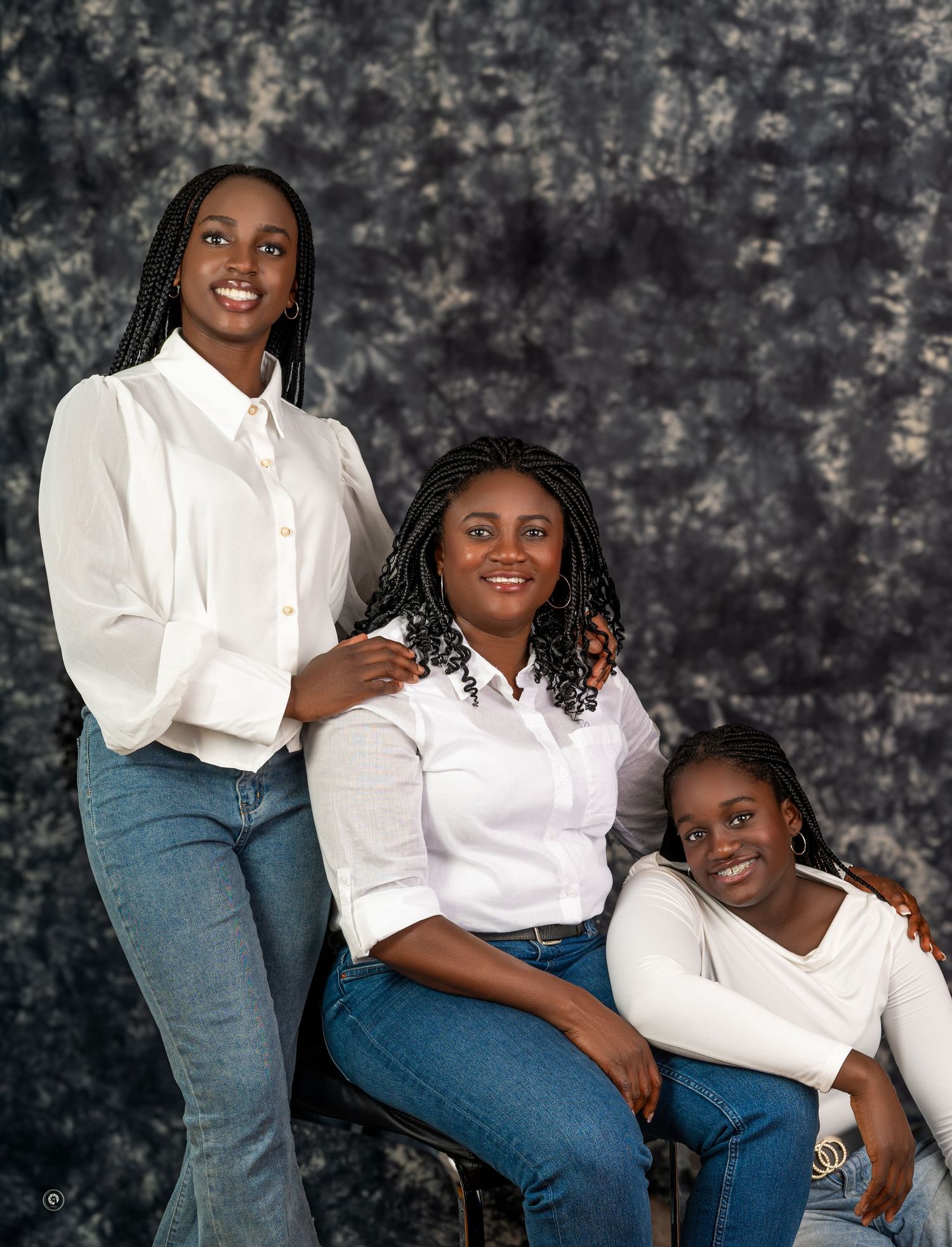 Family portrait session showing coordinated outfits of white shirts and blue jeans against a dark textured backdrop.