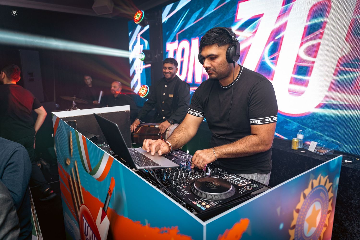 DJ performs at a nightclub with colorful neon lighting and electronic equipment setup.