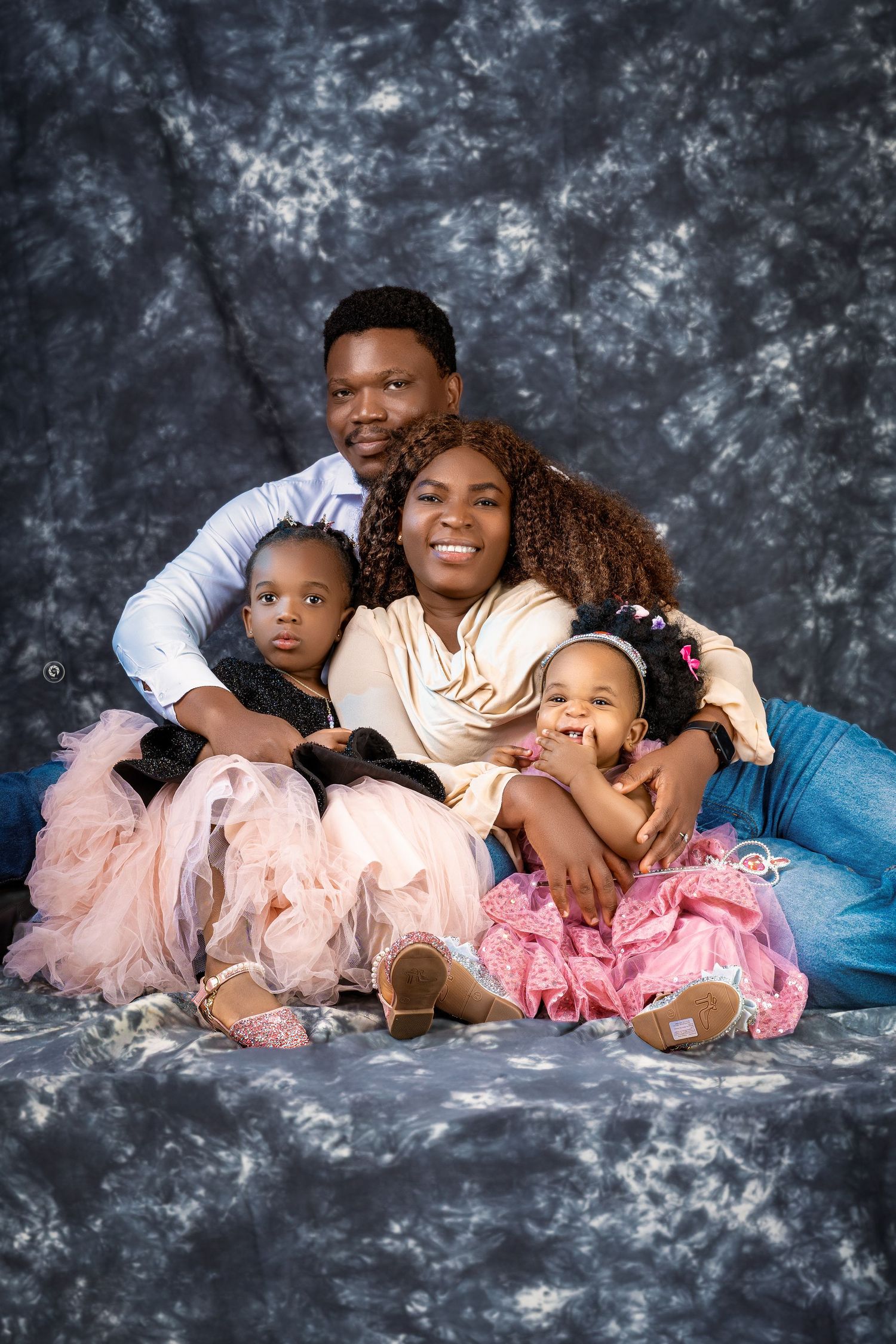 A family in coordinated pink and white outfits poses together on a gray backdrop for a series of portraits.