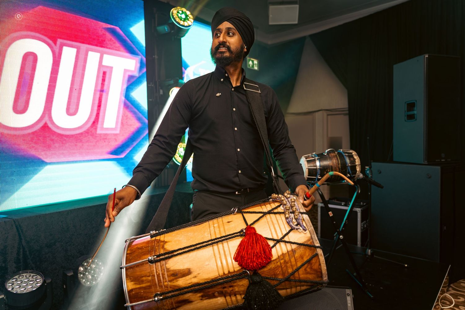 Musicians perform on stage with drums and instruments under vibrant red and blue lighting at a live concert venue.