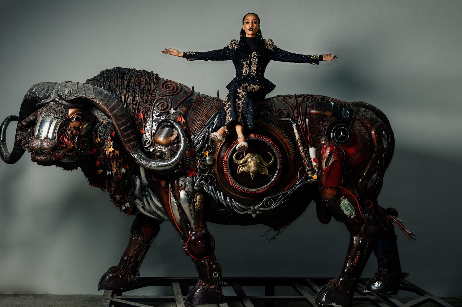 A figure stands atop a large mechanical steampunk-style horse sculpture with ornate metallic details in a dark setting.