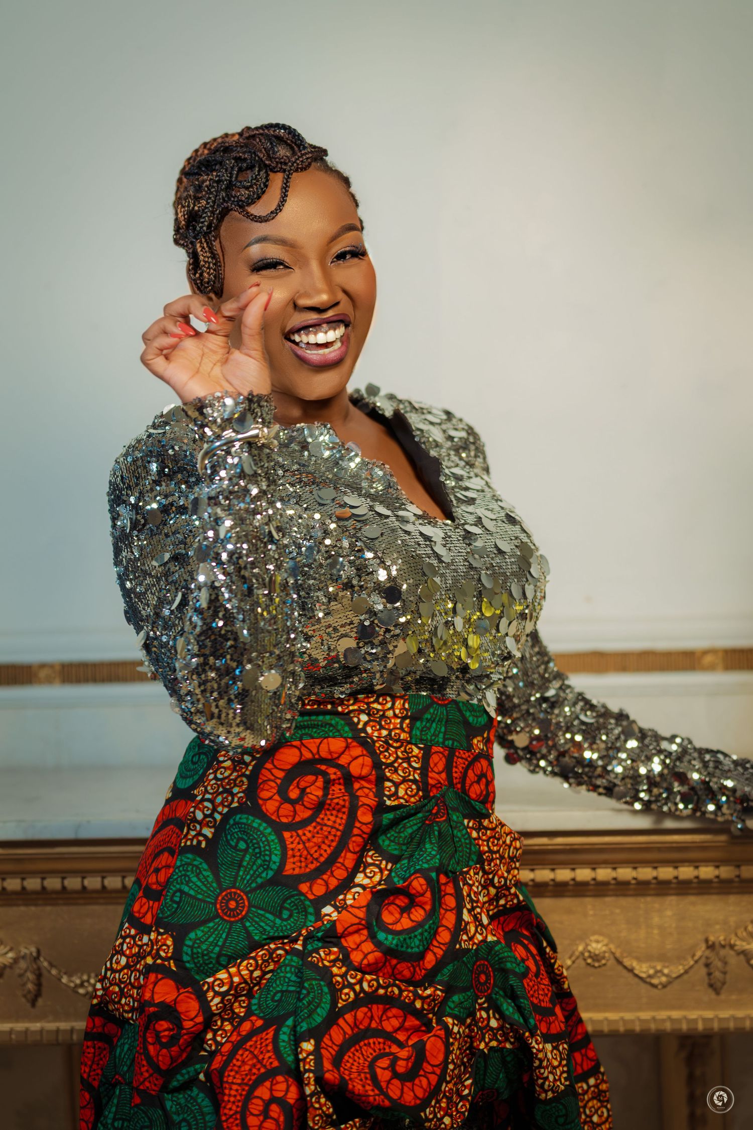Smiling woman in sequined silver top and colorful African print skirt posing joyfully indoors.