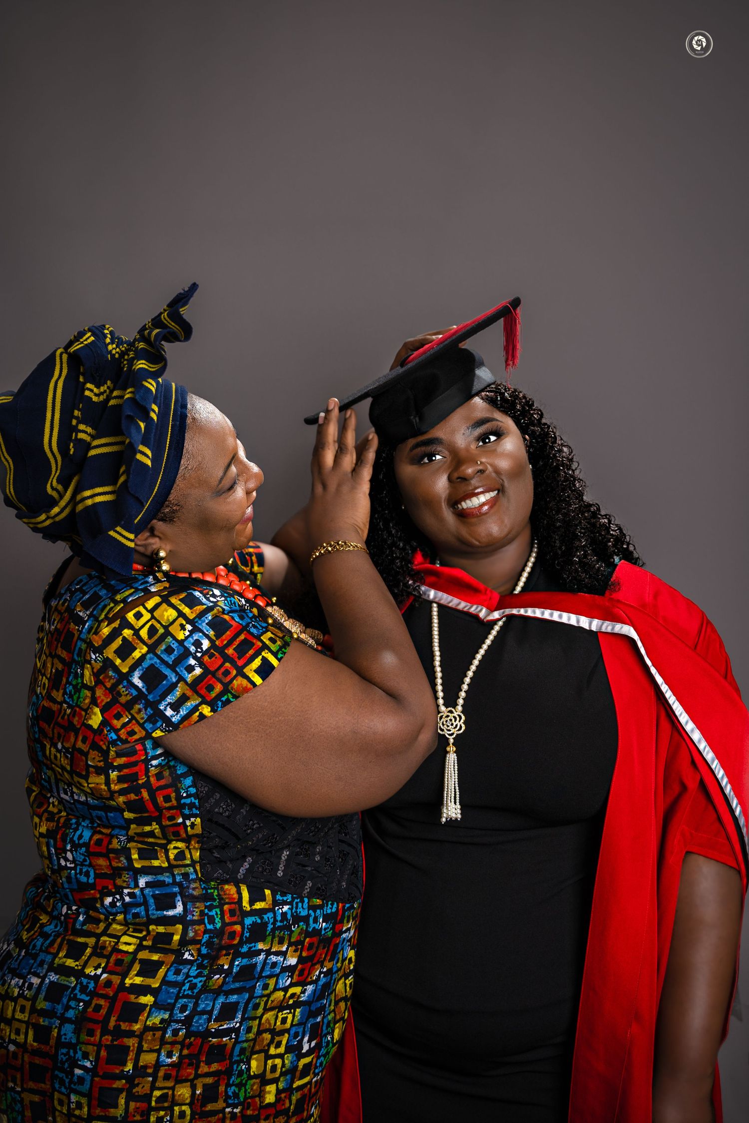 Two women in colorful African headwraps and contrasting outfits pose playfully together in a photo series.