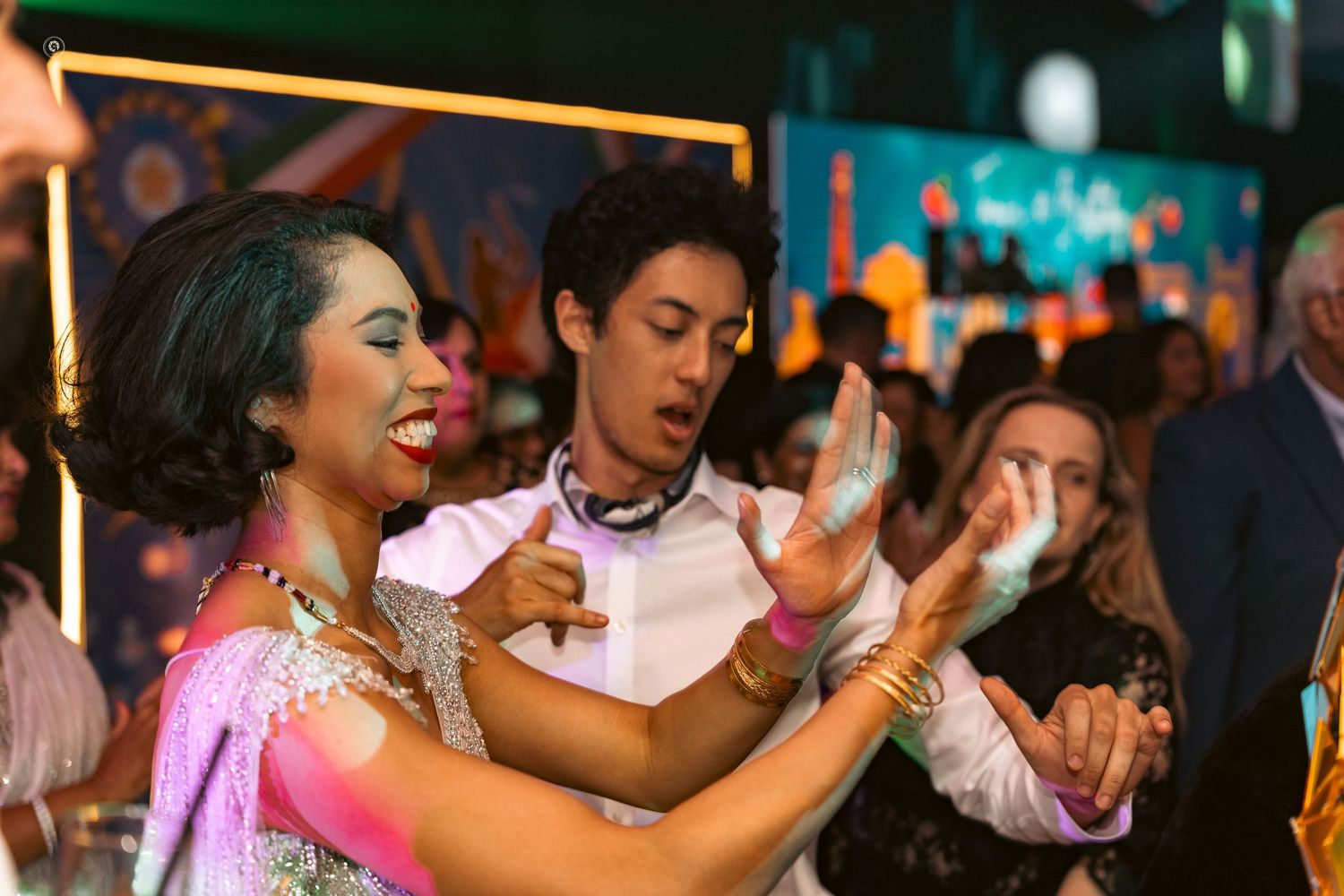 Wedding guests dancing and celebrating on a colorful dance floor at an evening reception.