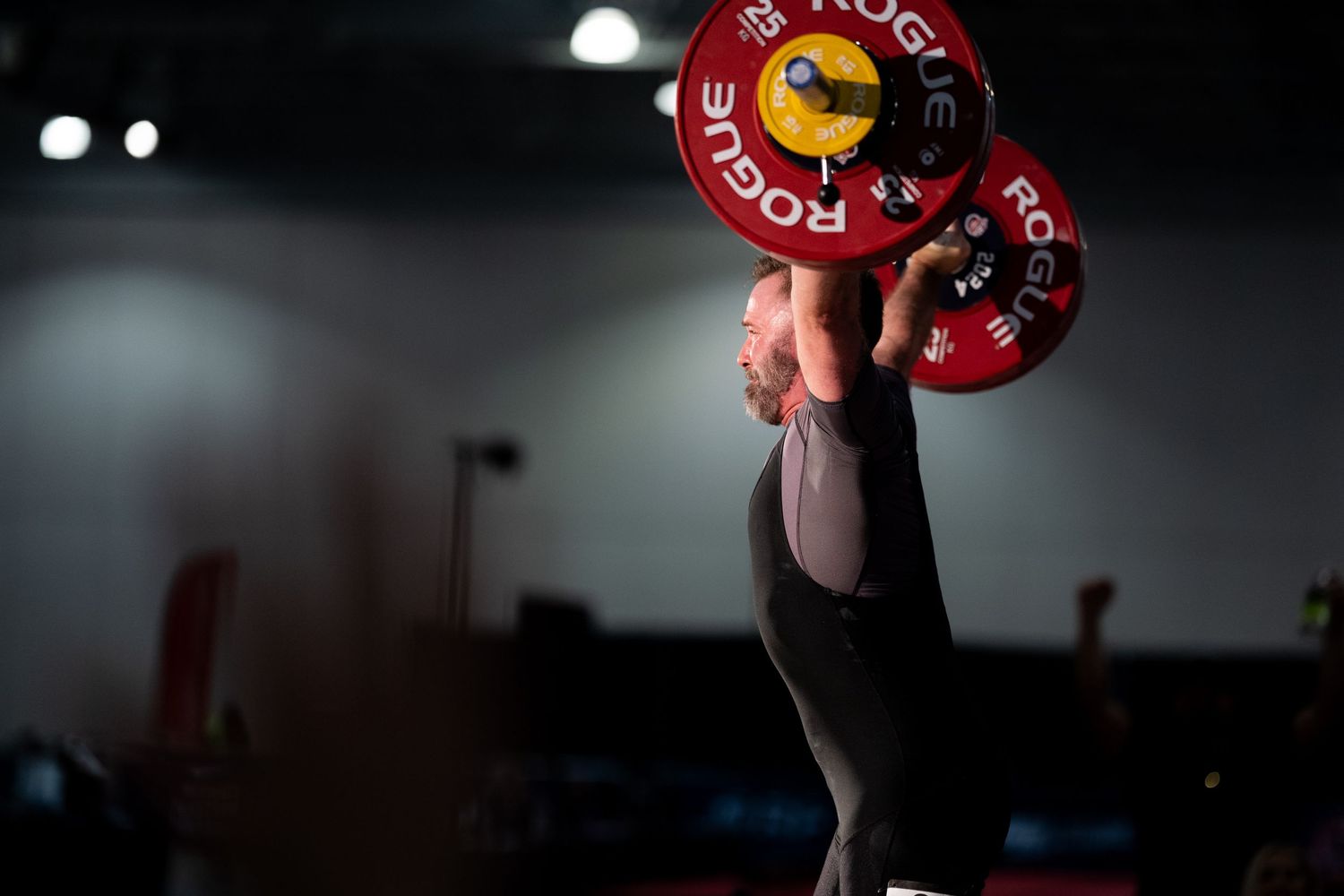 Dramatic low-light photo of red weight plates being lifted in a gym setting.