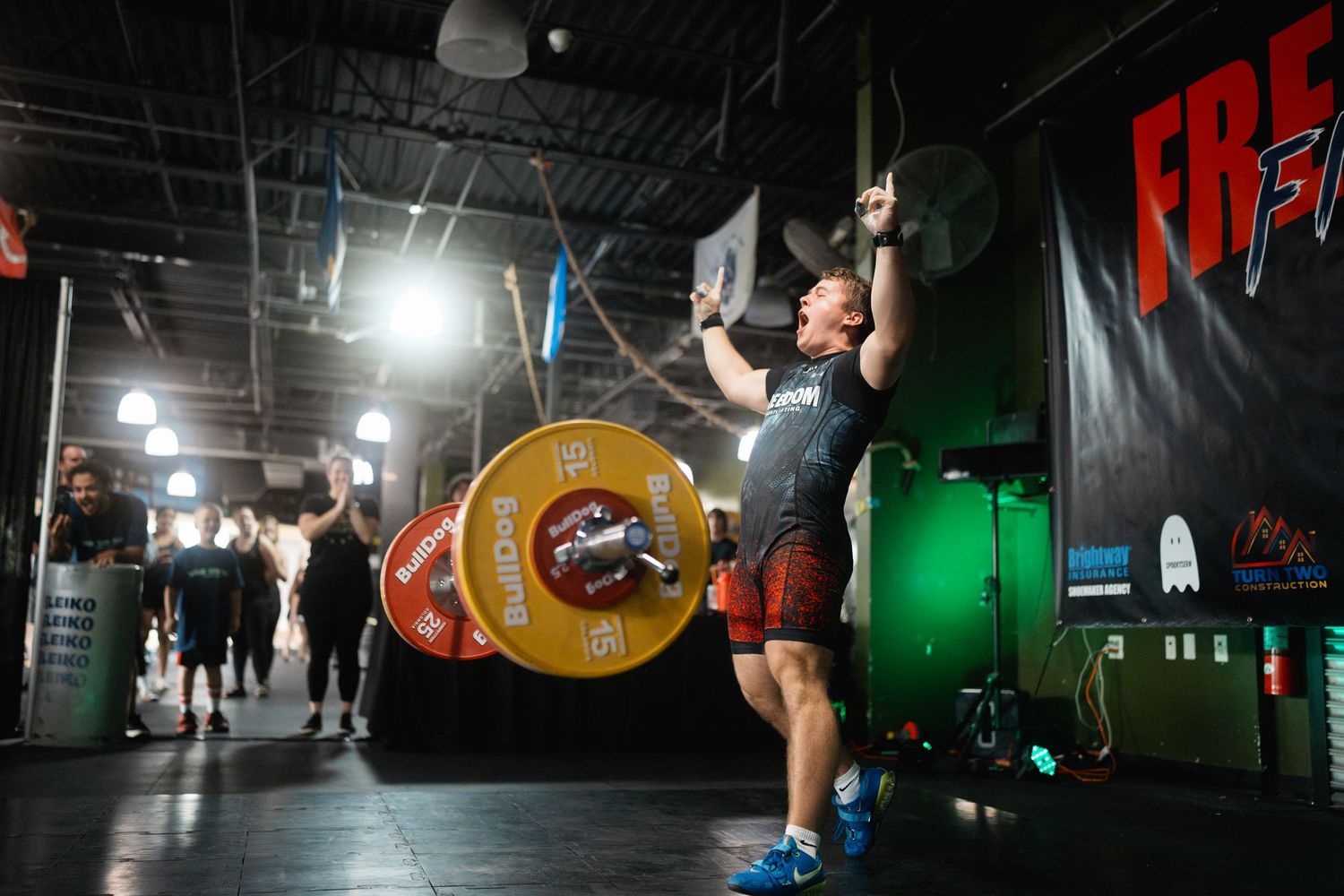 Athlete performing an Olympic lift with colorful weight plates in a dimly lit gym setting.