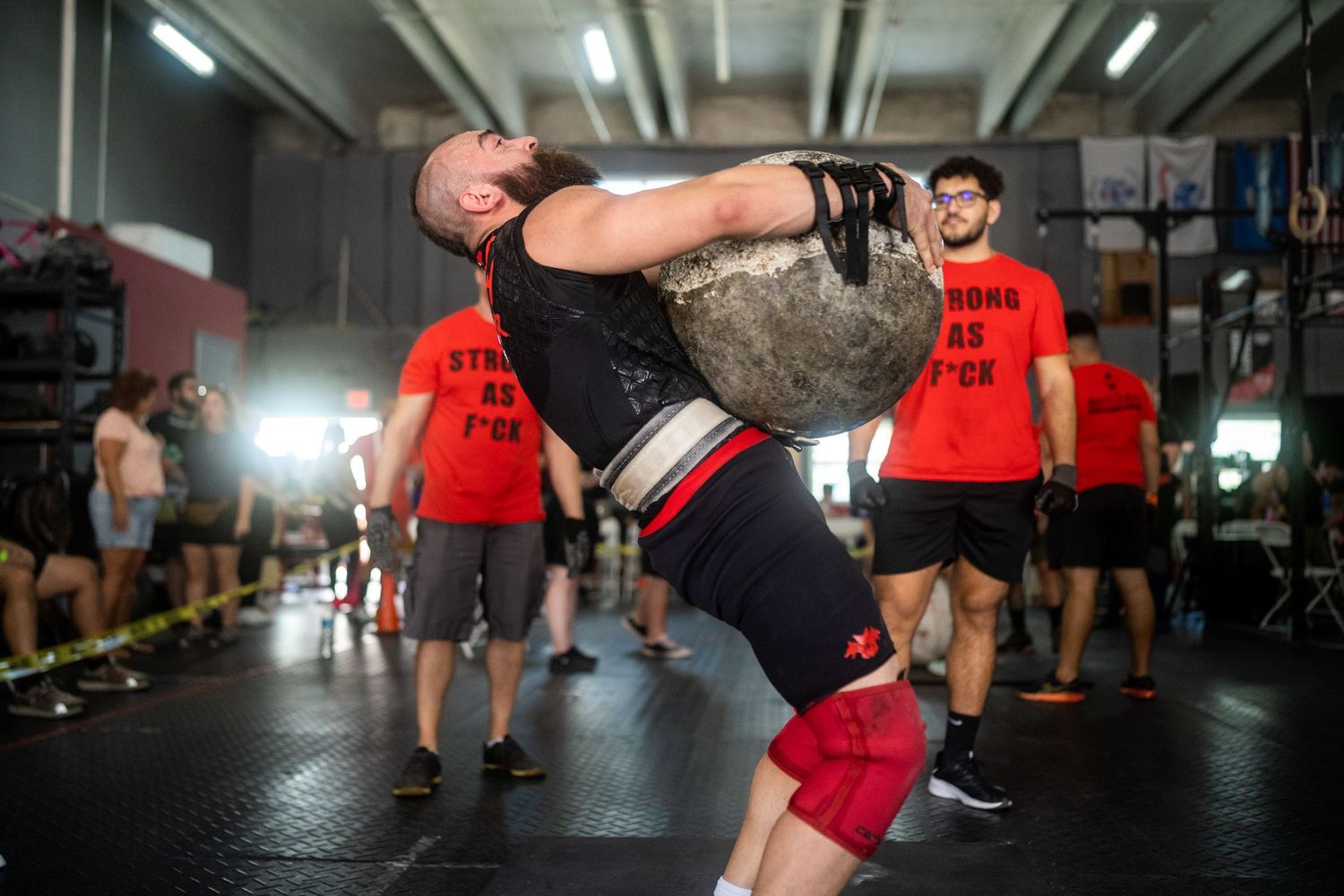 Athlete performing a stone lift during a strength training session in a gym.